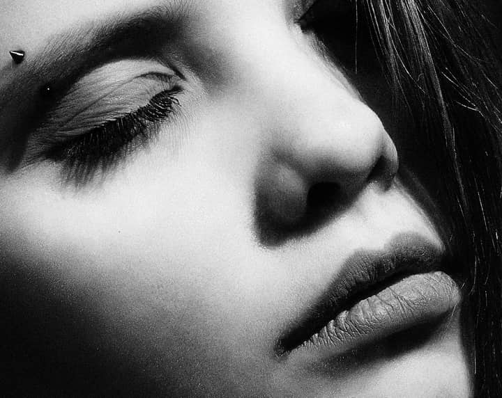 Artistic close-up black and white portrait of a woman with an eye piercing.