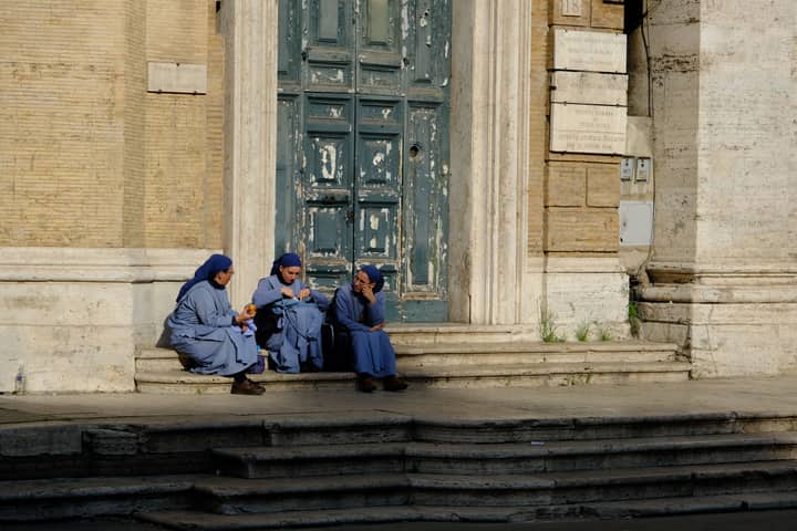 A tranquil scene of nuns in blue habits resting on church steps in Rome, Italy.