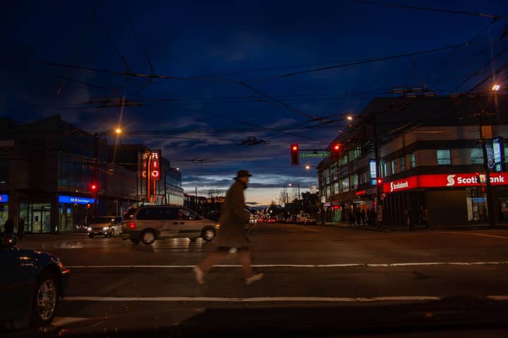 A dynamic night scene of a Vancouver intersection with pedestrians, cars, and bright city lights.