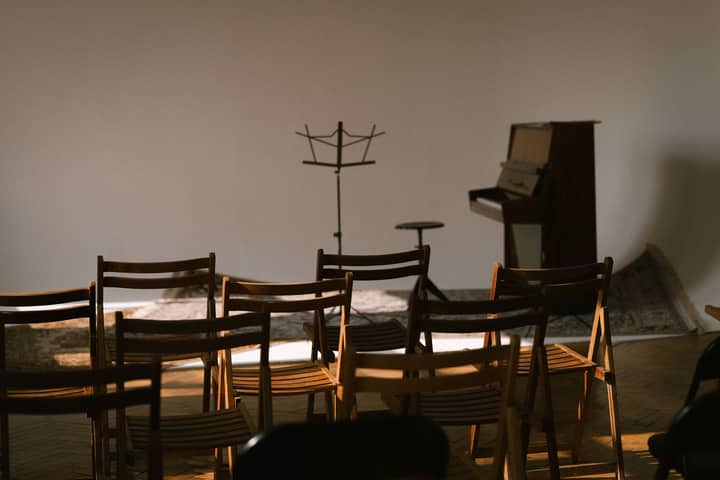 An empty music room with wooden chairs, a piano, and a sheet music stand ready for a performance.