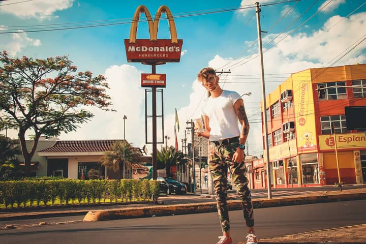 A fashionable man poses in an urban area near a McDonald's sign on a sunny day.