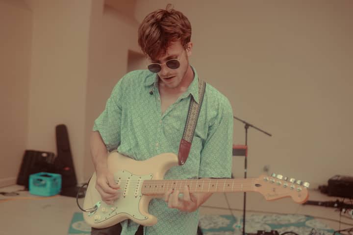 Young male guitarist in a green shirt playing electric guitar indoors.