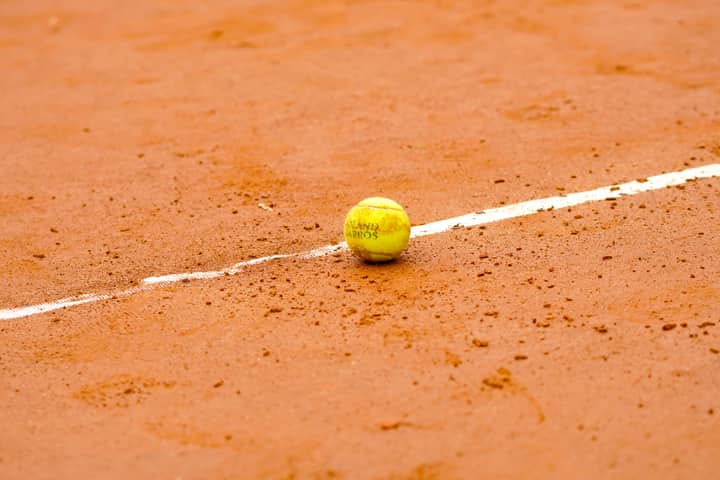 Tennis ball resting on a clay court, marked by a white line, ideal for sports themes.