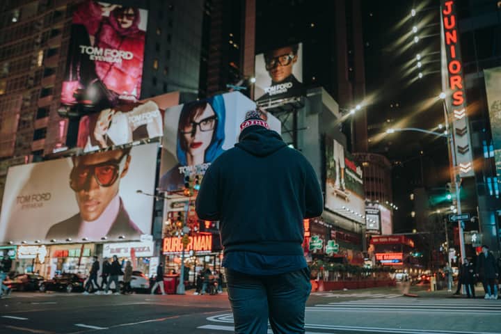 Street scene with a man standing in a vibrant city at night, surrounded by billboards.