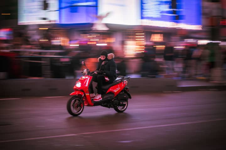 A person rides a red scooter through a vibrant city street at night.