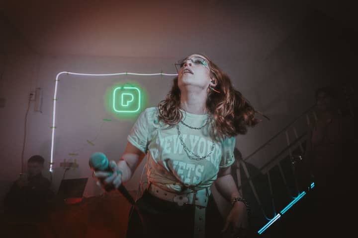 Singer performing with dynamic energy at a neon-lit indoor concert stage.