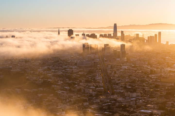 Aerial view of a foggy San Francisco skyline at sunrise, highlighting iconic skyscrapers and urban landscape.