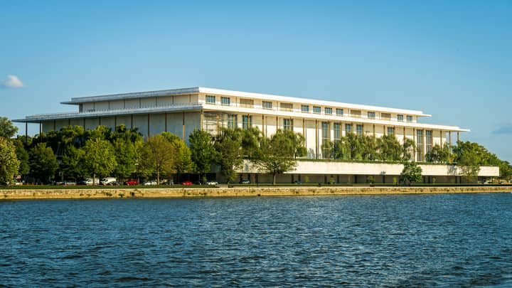Captivating view of the Kennedy Center beside the Potomac River with lush greenery in summer.