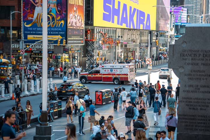 A vibrant view of Times Square, New York City, featuring a busy street with people and an FDNY ambulance.