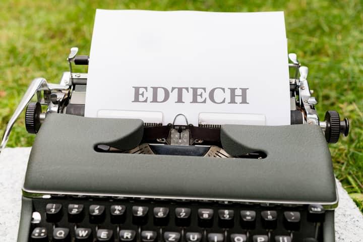 A vintage typewriter displays 'EdTech' on paper, set outdoors on grass.