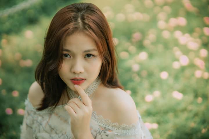Elegant young woman with red hair in a lush floral garden setting.