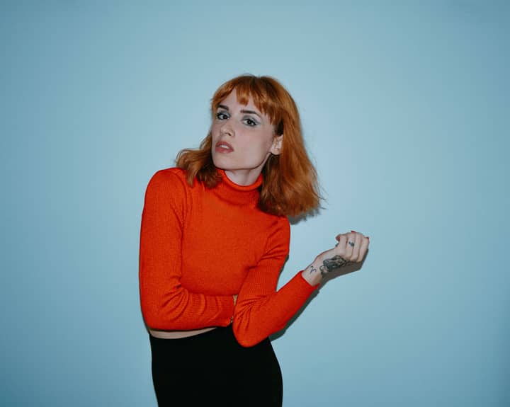 Portrait of a stylish adult woman in a red turtleneck sweater against a blue background.