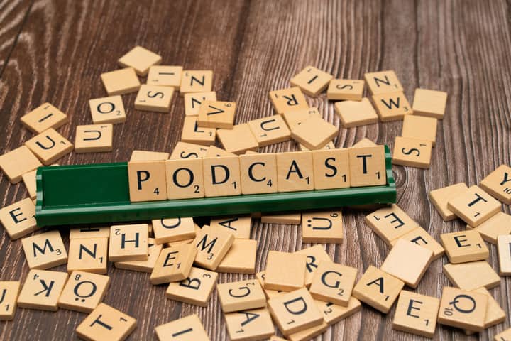Wooden letter tiles on a board spelling the word 'Podcast', symbolizing digital media and creativity.