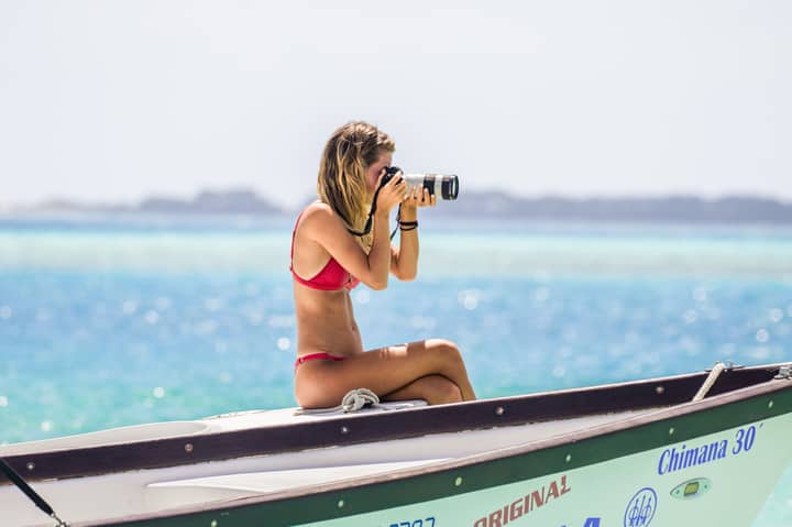 A woman in a bikini sits on a boat, taking photos of the scenic ocean view.