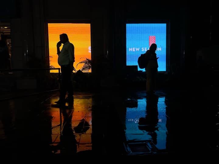 Two silhouettes in a dark corridor with vibrant billboard reflections creating a cinematic urban mood.