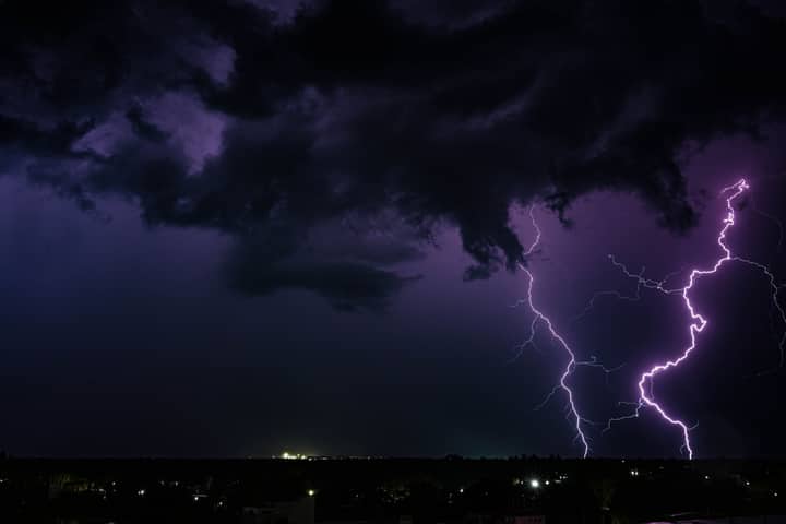 A powerful thunderstorm with dramatic lightning strikes over a city at night in India.