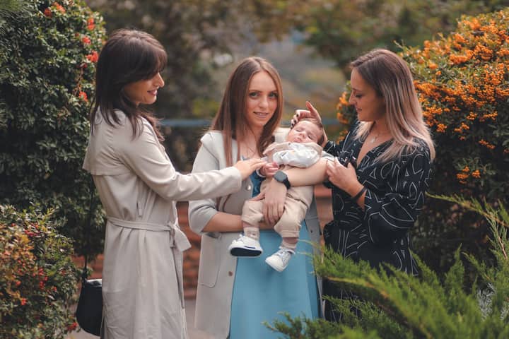 Three women joyfully admiring a newborn in a lush garden. A harmonious blend of nature and family bonding.