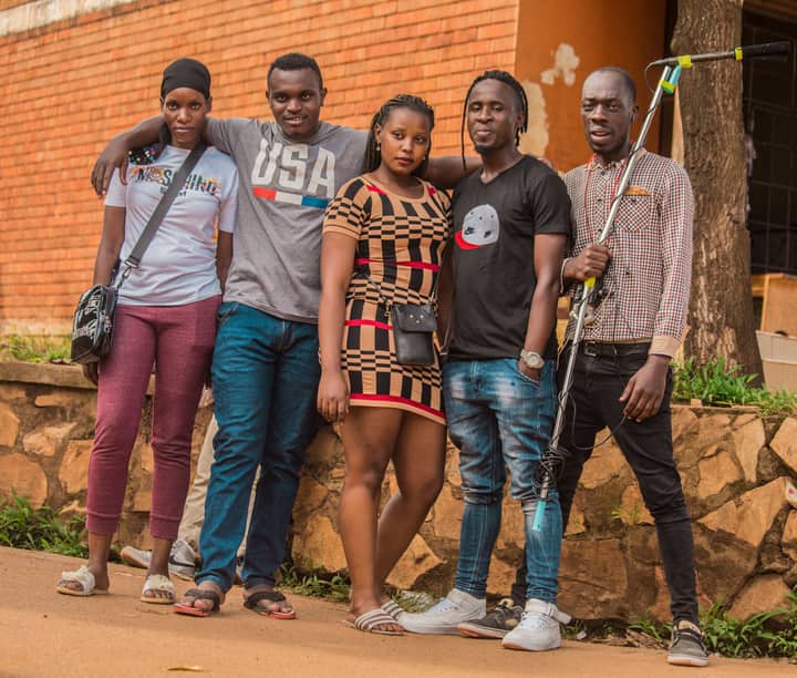 A group of friends standing together smiling outdoors in Uganda, enjoying a sunny day.