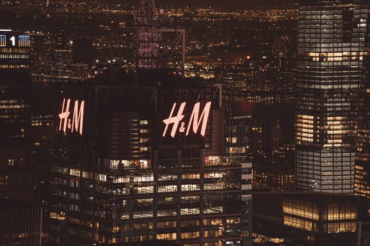 High-angle view of illuminated skyscrapers in New York City at night, featuring H&M building lights.