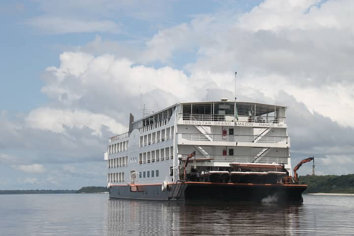 A luxurious cruise ship navigates the serene waters of the Amazon River under a cloudy sky.