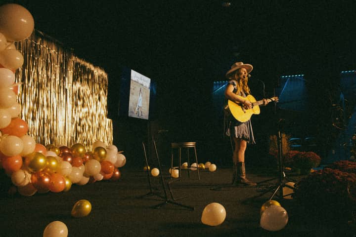 A woman playing guitar on stage decorated with balloons, creating a vibrant performance ambiance.