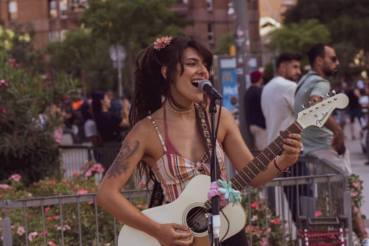 A female street musician performing with guitar in Barcelona cityscape.