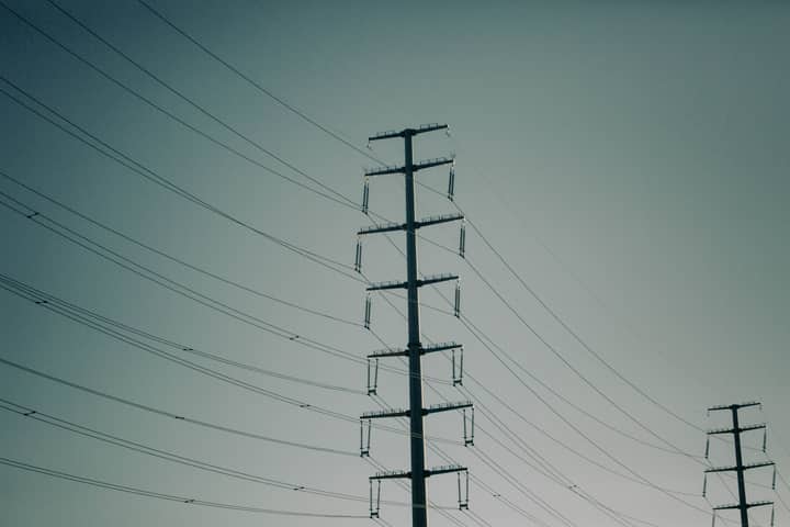 Silhouetted power lines against a muted sky, showcasing electrical transmission infrastructure.