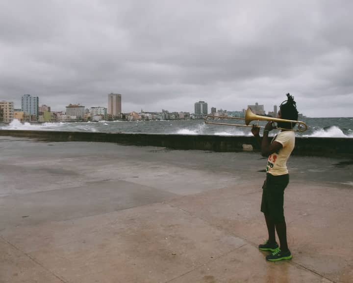 Young man playing trombone outdoors near the ocean on a cloudy day.
