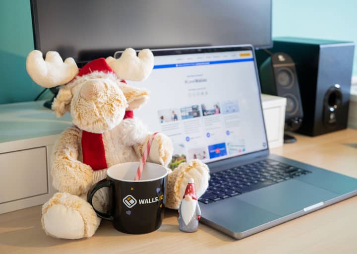 Home office setup with festive Christmas decorations, featuring a plush toy, black mug, and laptop.