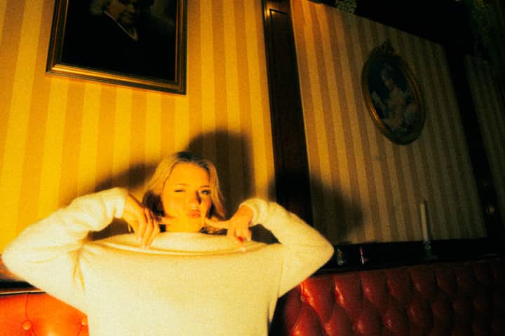 A playful blonde woman makes a face while sitting on a sofa in a cozy living room.