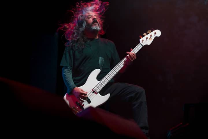 A passionate musician playing bass guitar with long hair flowing on stage.