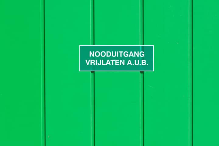 A green metal wall featuring an emergency exit sign in Dutch. Perfect for safety-themed graphics.