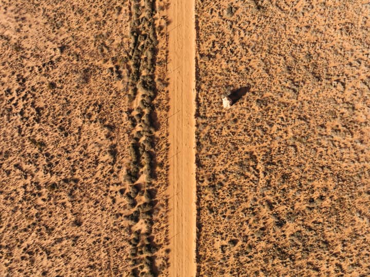 Aerial shot capturing a vast desert landscape with a prominent dirt road cutting through arid terrain.
