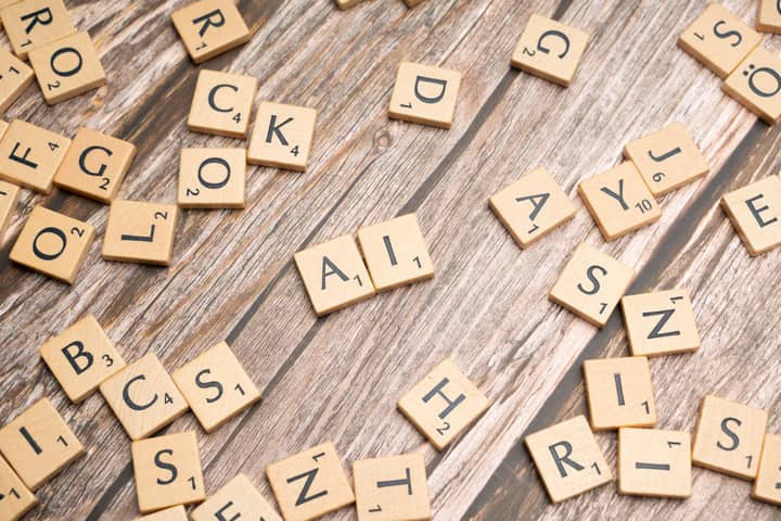 Wooden letter tiles scattered on a textured surface, spelling 'AI'.