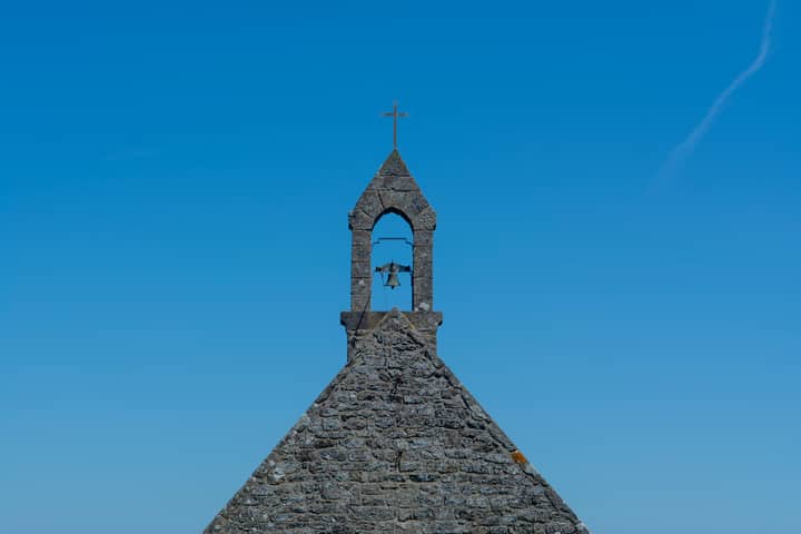 Serene view of a stone chapel bell tower against a clear blue sky, showcasing architecture.