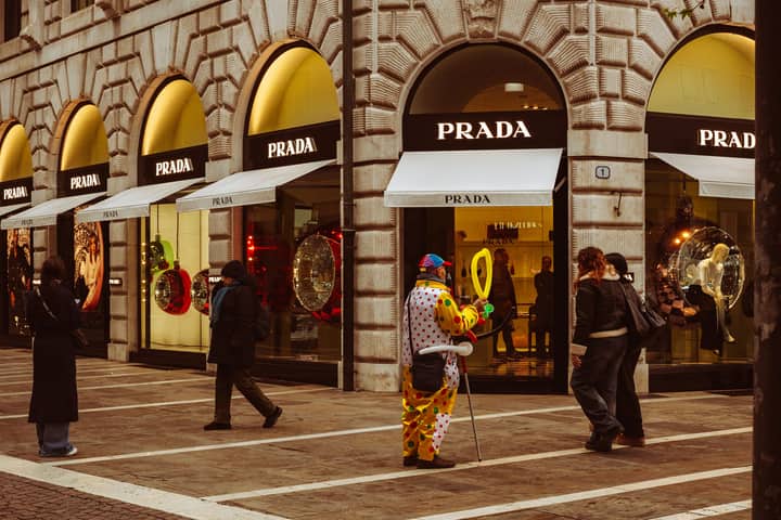 People passing by a vibrant clown entertainer outside a Prada store in Padova, Italy.