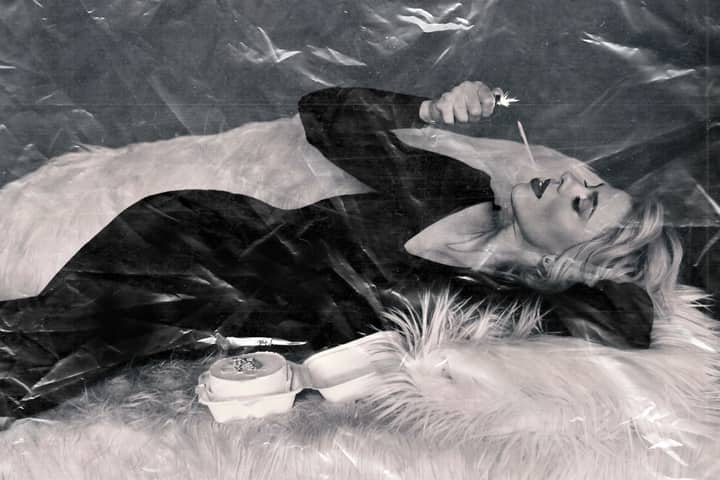 Stylish woman in vintage attire smoking, lying down in a black and white photograph.