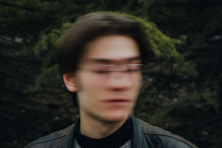 A blurred image of a young man with glasses outdoors, conveying motion.
