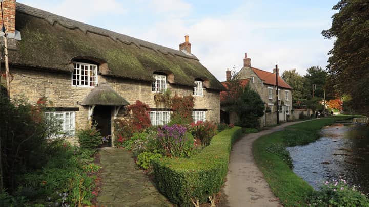Scenic view of thatched cottages beside a river in Thornton Dale, England.