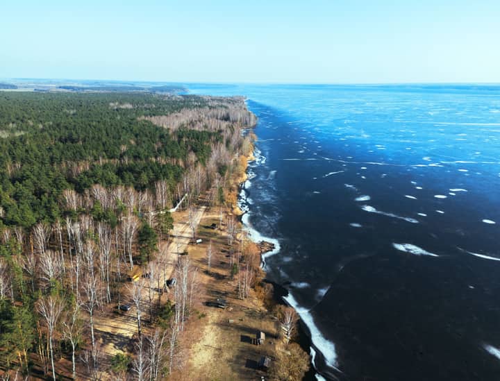 A stunning aerial view of a frozen lake contrasting with a lush forest along the coastline in Vileyka, Belarus.