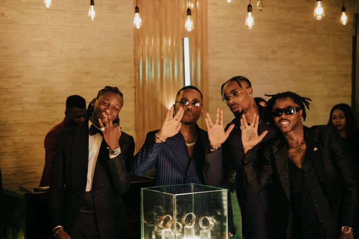 Group of stylish men in suits posing indoors with unique hand gestures, creating a vibrant party vibe.