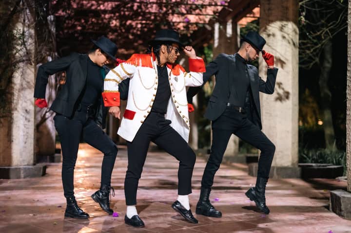 Three men in fashionable dance outfits and hats posing dramatically outdoors at night.