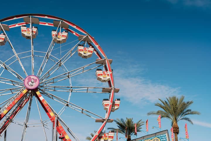 A vibrant ferris wheel and palm trees under a blue sky at Coachella, California.