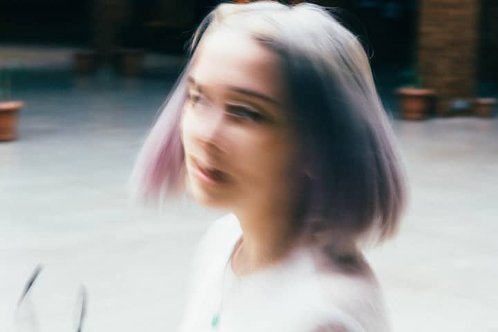 Dynamic blurred portrait of a young woman with dyed purple hair outdoors.