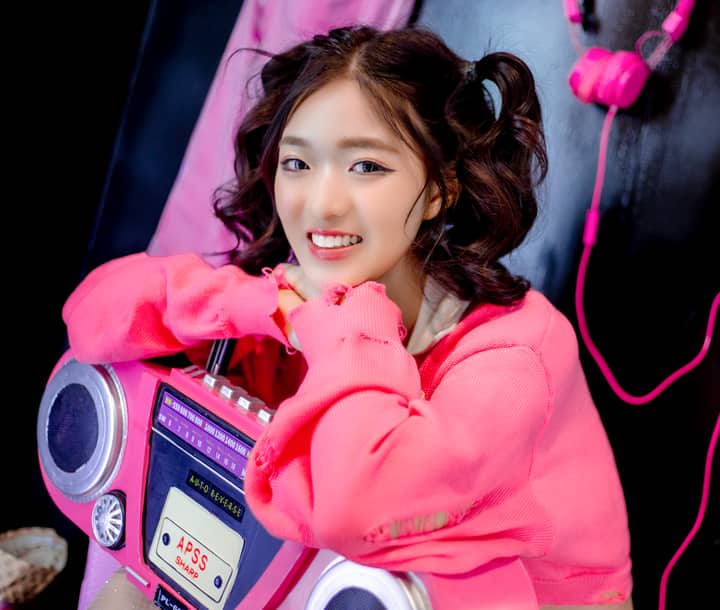 A young woman in bright pink fashion poses with a retro radio, smiling and vibrant.