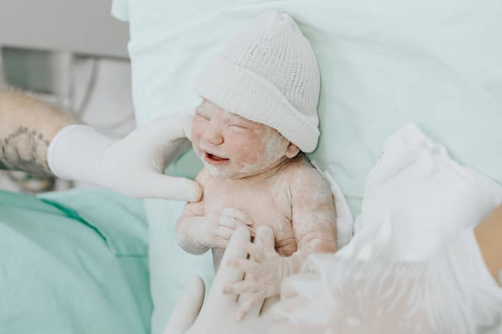 A newborn baby just delivered, attended by medical staff wearing gloves in a hospital setting.