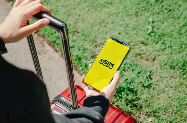 A person holds a smartphone showing an eSIM app while standing with luggage outdoors in Los Angeles.