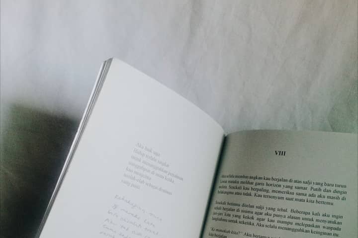 Open book with text on white surface, minimalist and monochrome style.