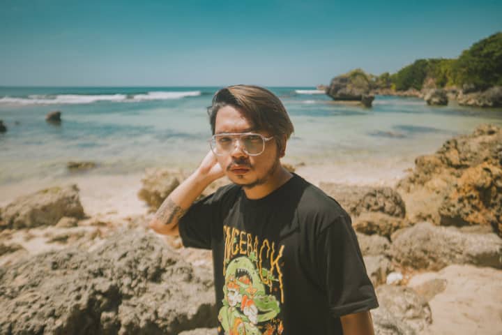 Young man with eyeglasses poses stylishly on a rocky beach in Bolinao, Philippines, under the bright summer sun.