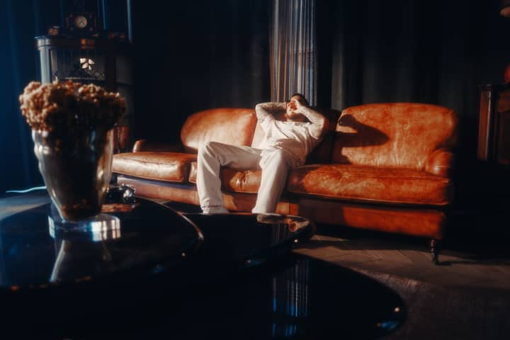 A man in a cozy living room relaxes on a vintage leather sofa, surrounded by warm ambient lighting.